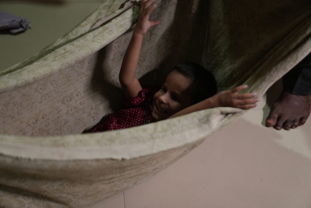 A young girl sitting in a hammock and smiling.