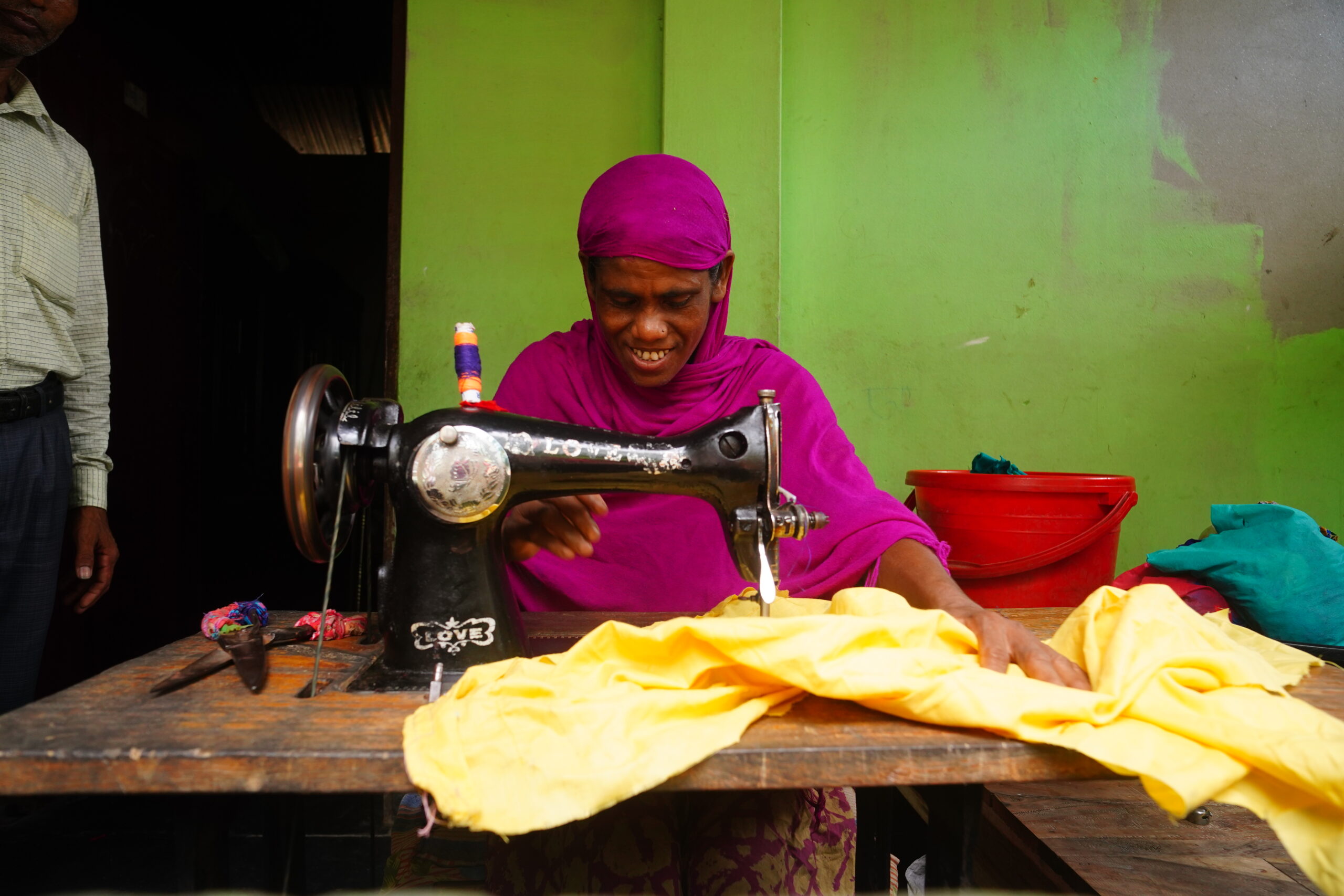 A woman wearing a purple head scarf working at a sewing machine.