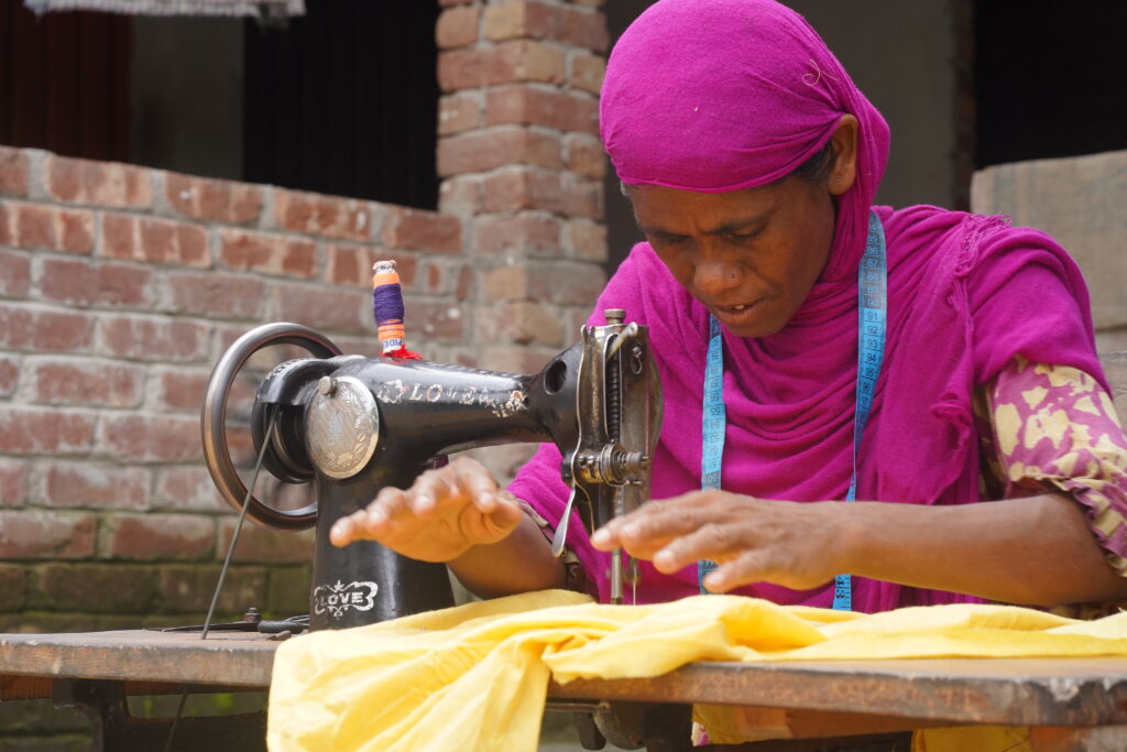 A woman wearing a purple head scarf working at a sewing machine.