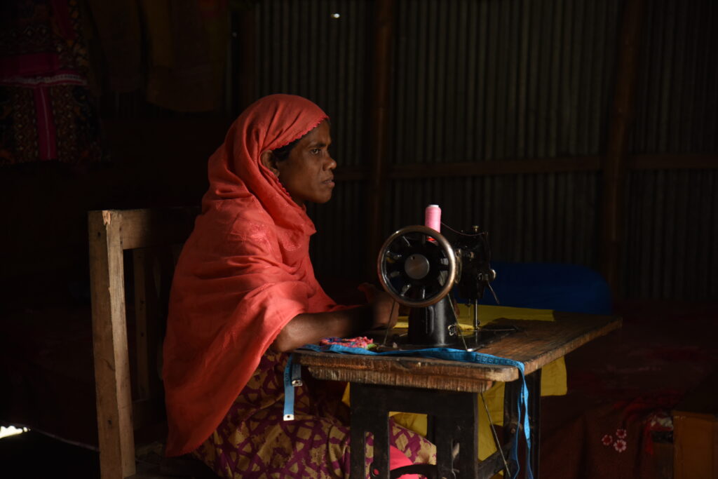 A woman wearing a orange head scarf working at a sewing machine.