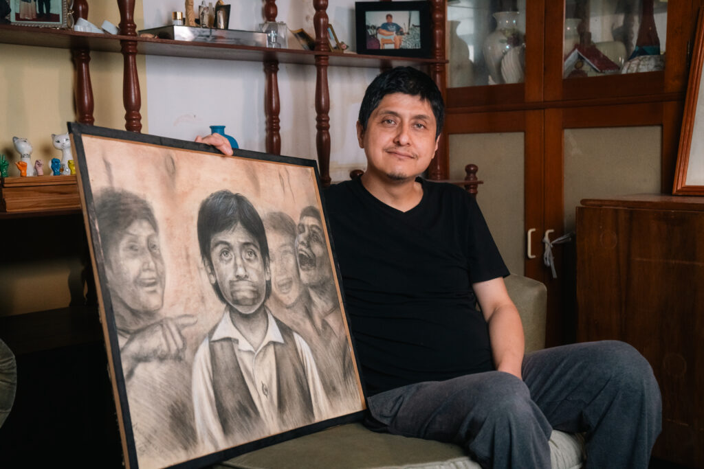 A man sitting on a sofa with a drawing of people pointing at a person silenced by tape on his mouth.