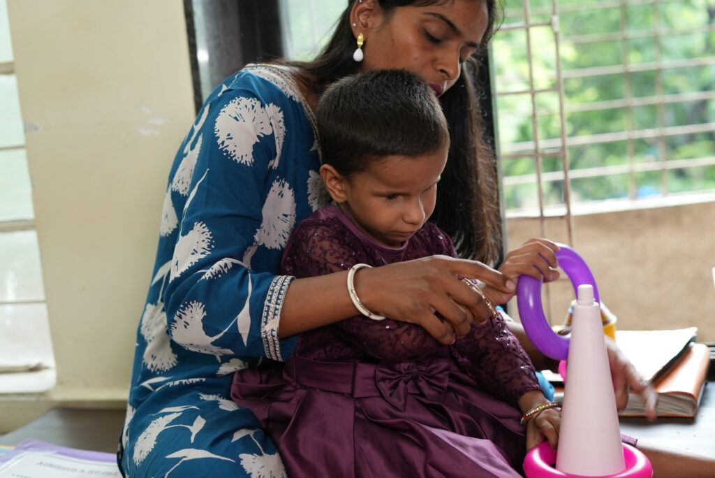 A young blind girl playing with toys and sitting with a woman.