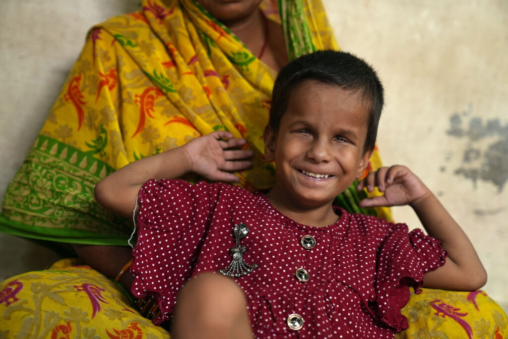 A young blind girl smiling and sitting with a woman.