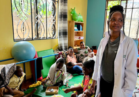 A support assistant looks at the camera as children play behind her