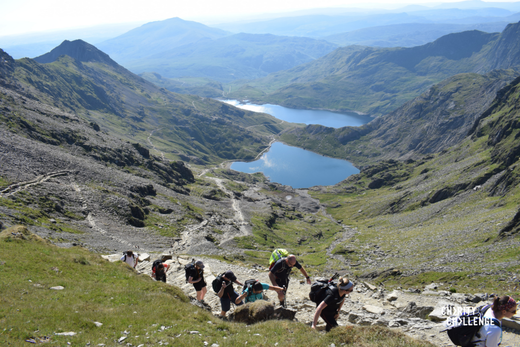 Hikers scaling a peak with lakes in the background.