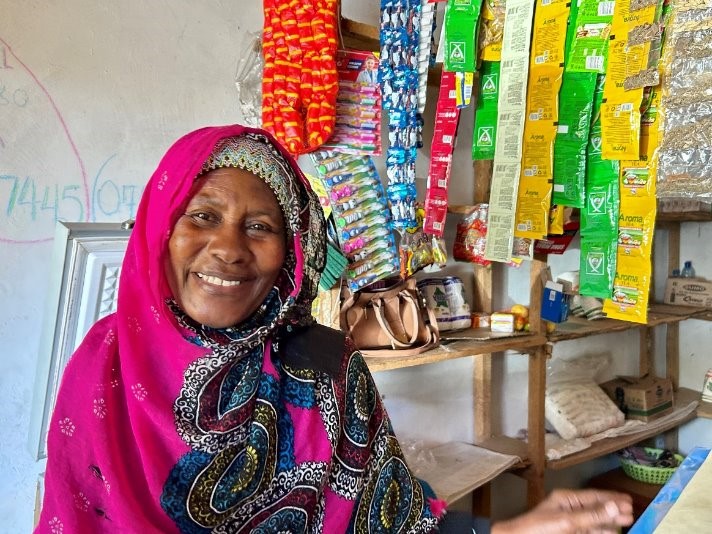 A smiling woman  stands proudly in front of her shop